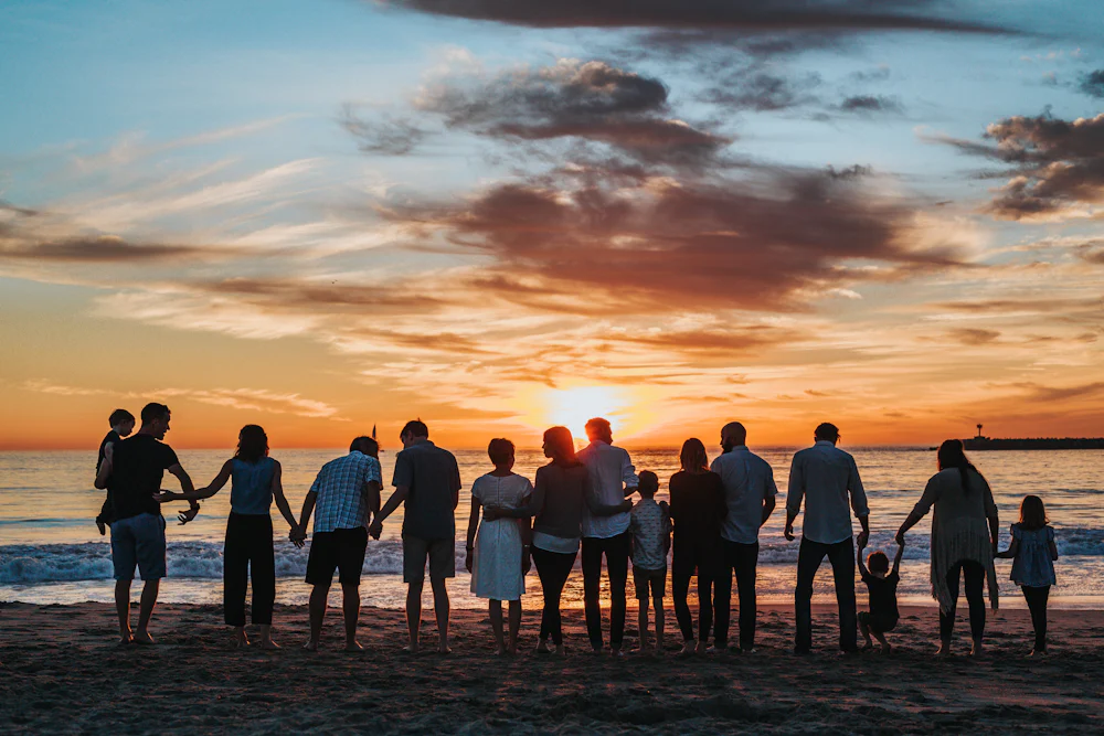 Grupo de familias tomadas de la mano frente al mar durante el atardecer