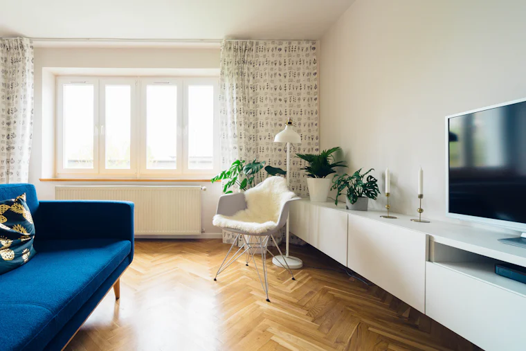 Sala luminosa con sofá azul, piso de madera y ventanales